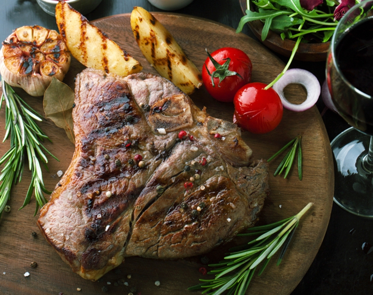 Grilled meat T-Bone with vegetables, spices and glass of wine on a wooden background